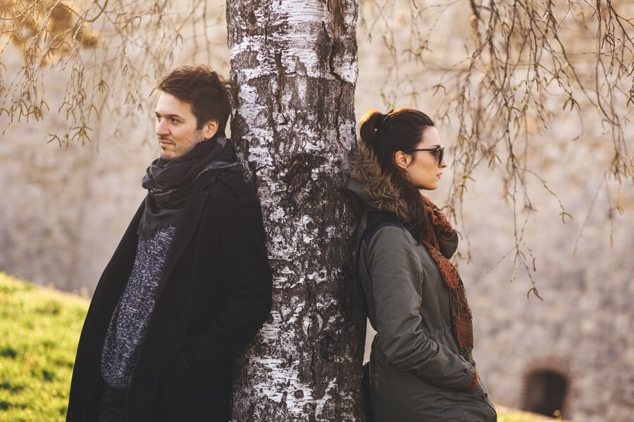 A married couple standing away from each other on opposite sides of a tree